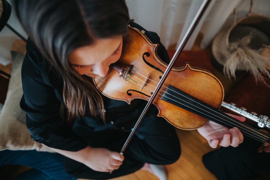 A young musician playing the violin indoors, focusing on the instrument. The natural lighting and intimate setting emphasize the performers dedication and the violins beauty in a serene atmosphere.