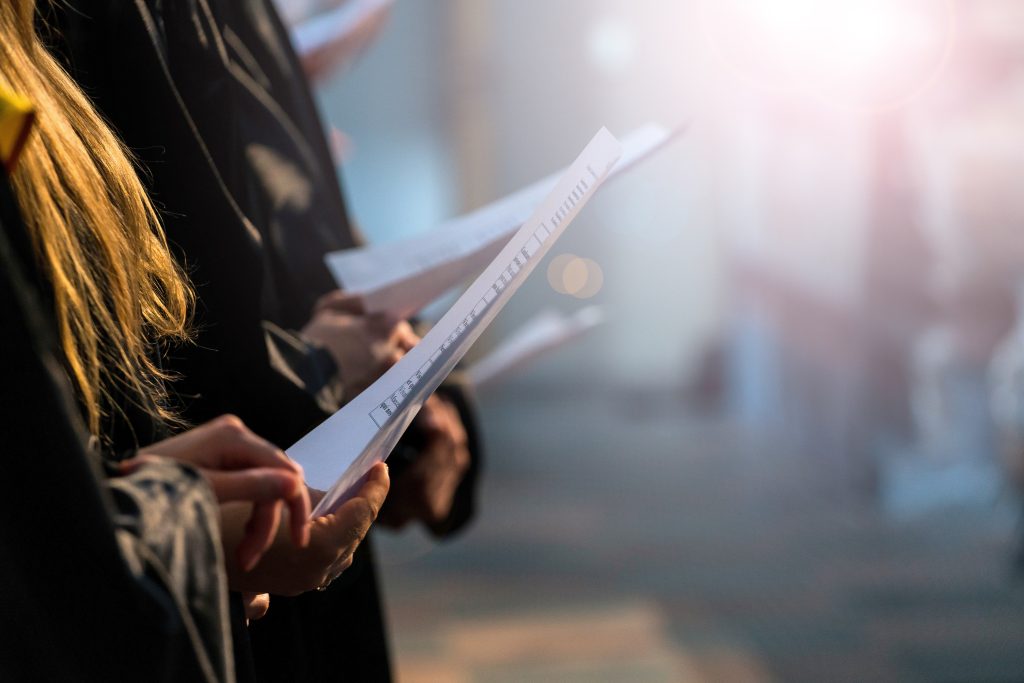 Choir singers holding musical score and singing on student graduation day in university, college commencement