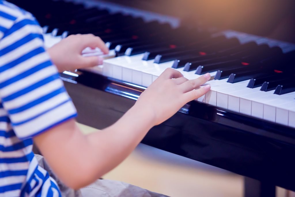 Selective focus to kid fingers and  piano key to play the piano. There are musical instrument for concert or learning music. Close up hand of child musician playing the piano on stage