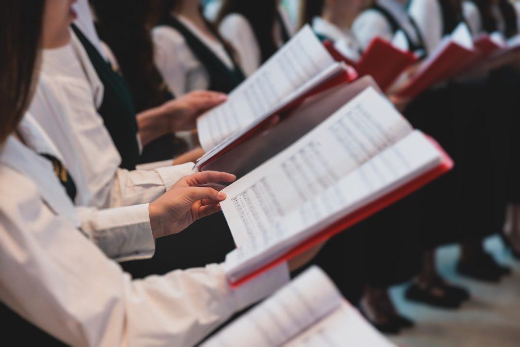 Church choir concert in cathedral, choral artists singing, group of European boys and girls singing in a chorus, students and choristers in white and green uniform performing on stage with conductor