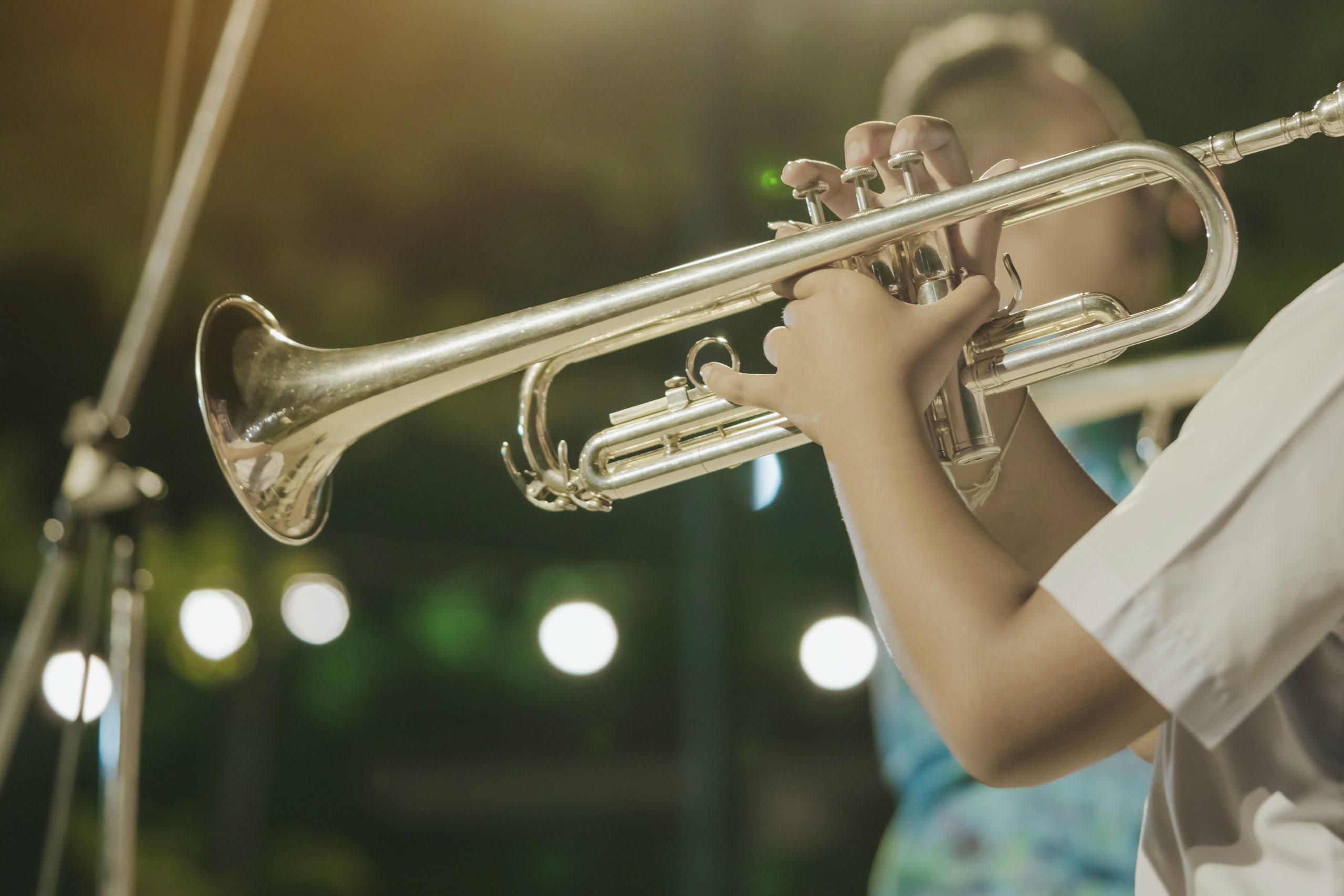 Male student with friends blow the trumpet with the band for performance on stage at night.